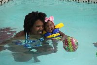 Black mother and baby daughter in the pool playing with a ball.