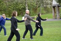 4 adults practice Wild Goose Qigong in a park.