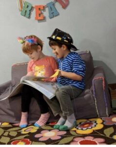 Little Laurelhurst Preschool - Children reading book on mini couch